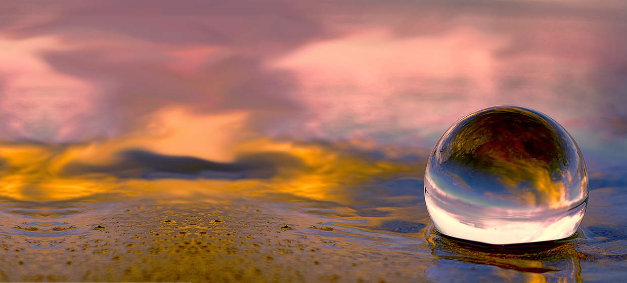 Home page slider image showing a summer sunset displayed through a transparent glass ball on the beach sand