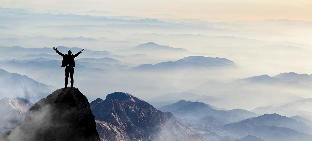 Home page slider image showing man on top of mountain with arms triumphantly thrown in the air